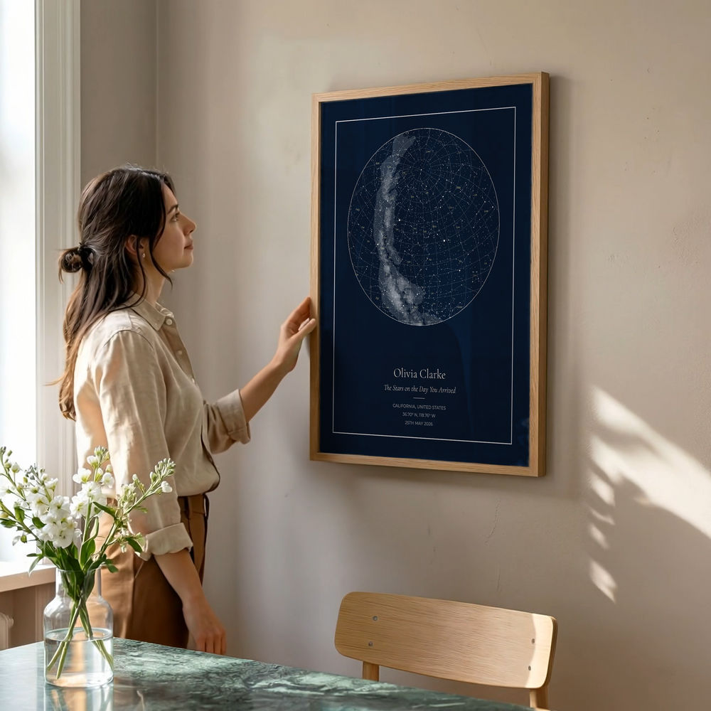 Woman looking at a framed star map on a wall in a room with natural light.