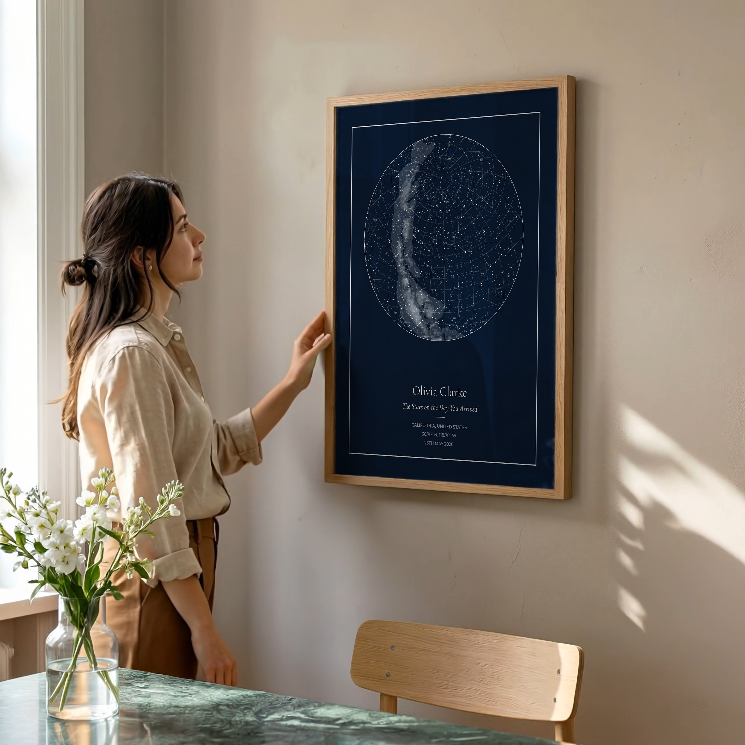 Woman looking at a framed star map on a wall in a room with natural light.