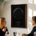 Framed star map poster on a wall with people sitting at a table below it.