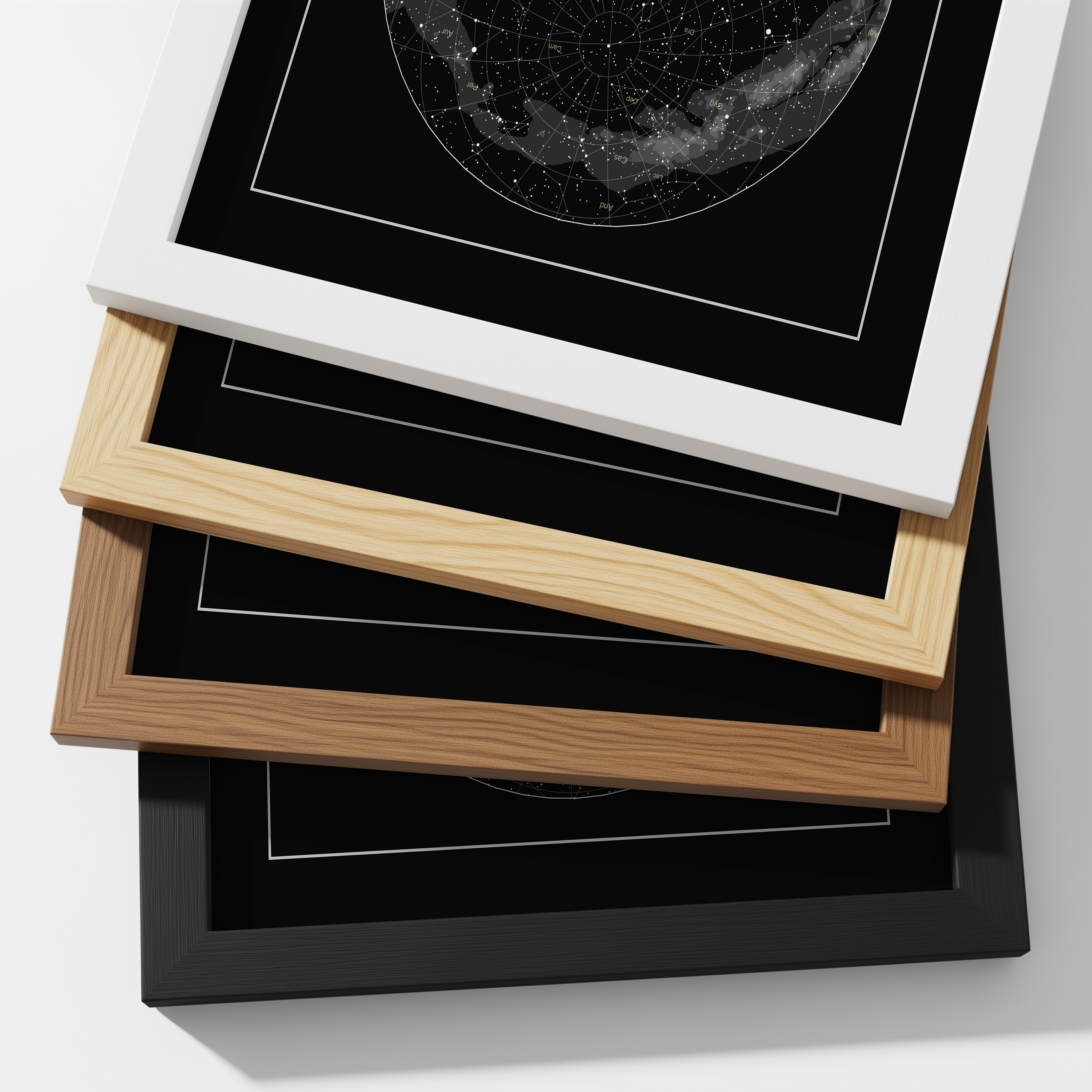 Stack of framed star maps with different frame colors on a white background